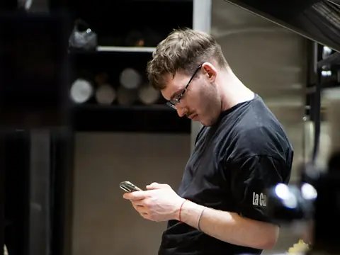 A cook checking his phone between tasks in a restaurant kitchen